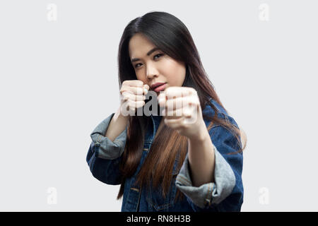 Portrait of serious beautiful brunette asian young woman in casual blue denim jacket with makeup standing with boxing fist and looking at camera . ind Stock Photo