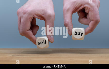 Hands are holding two cubes with the words 'sell' and 'buy'. One hand rises the cube with the word 'buy'. Stock Photo