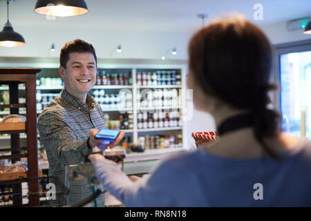 Male Customer Making Contactless Payment For Shopping Using Mobile Phone In Delicatessen Stock Photo