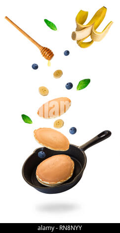 Homemade pancakes, blueberries and banana flying into iron skillet isolated on white background. Stock Photo