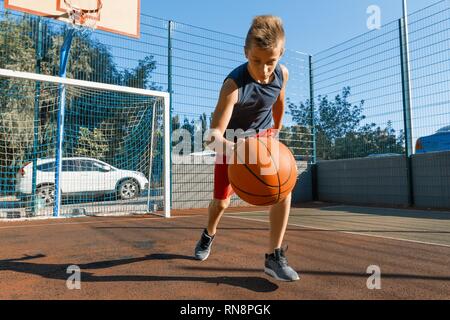 Caucasian teenager boy street basketball player with ball on outdoor city basketball court. Stock Photo
