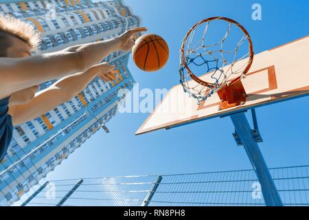 Caucasian teenager boy street basketball player with ball on outdoor city basketball court. Stock Photo