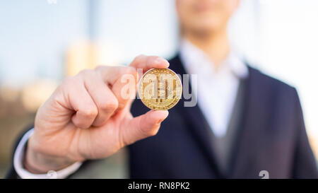 Bitcoin cryptocurrency coin in a young businessman hand. Disruptive blockchain technology concept and transfer of wealth. Stock Photo