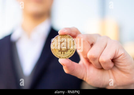 Bitcoin cryptocurrency coin in a young businessman hand. Disruptive blockchain technology concept and transfer of wealth. Stock Photo