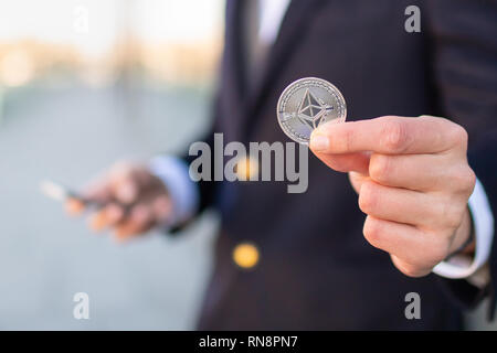 Ethereum cryptocurrency coin in a young businessman hand. Disruptive blockchain technology concept and transfer of wealth. Stock Photo