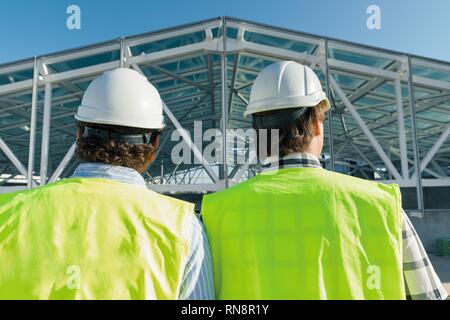 Male builders on roof of construction site,back view. Building, development, teamwork and people concept. Stock Photo