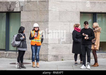 MONTREAL, CANADA - NOVEMBER 7, 2018:Young woman wearing safety PPE equipment, a helmet and an orange visibility vest discussing during her break with  Stock Photo