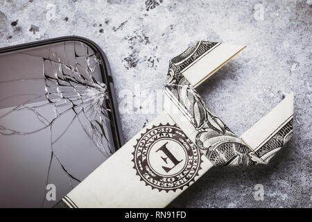 Broken cell phone glass and a dollar in the form of a key, as the concept of the cost of repairing a mobile device, close-up Stock Photo