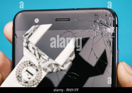 Broken screen of the phone in hand and dollar in the form of a key, as a concept on cost of repairing a mobile device, close-up Stock Photo