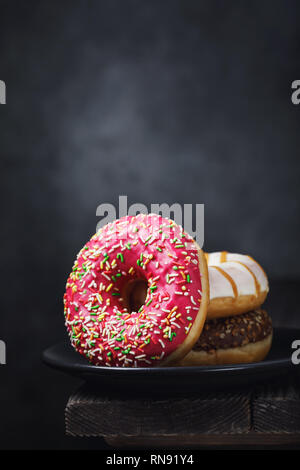 Several donuts in a black ceramic plate on a wooden table with copy space Stock Photo