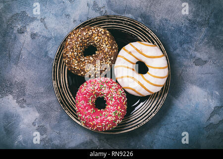 Three donuts with strawberry, chocolate and caramel in a plate on table, top view Stock Photo