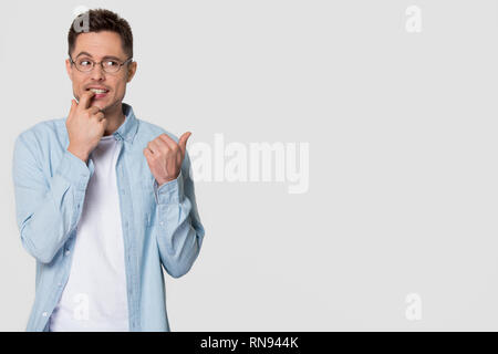 Nervous doubtful young man biting nails wondering pointing at copyspace Stock Photo