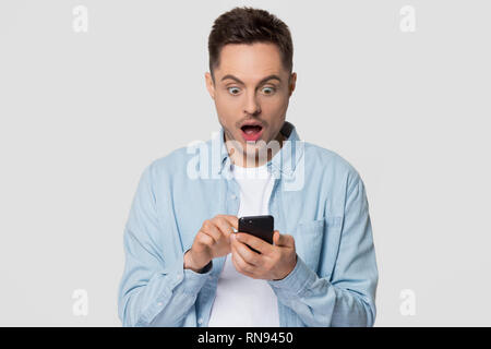 Surprised guy holding cellphone looking at phone shocked by news Stock Photo