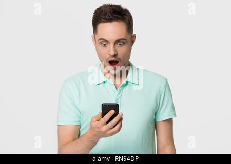 Shocked young man holding phone astonished by social media news Stock Photo