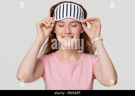 Smiling happy young redhead woman wearing striped sleeping eye mask Stock Photo