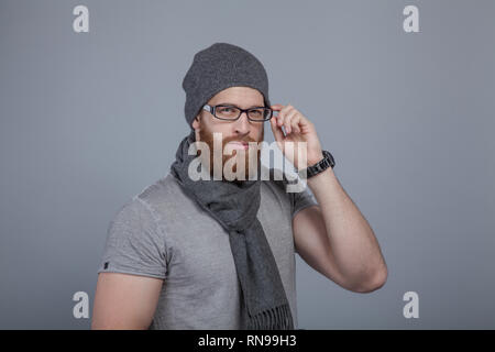 A serious bearded man holds one-handed glasses and looks at the camera. Stock Photo