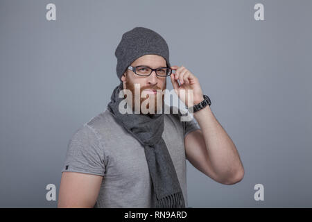 A serious bearded man holds one-handed glasses and looks at the camera. Stock Photo