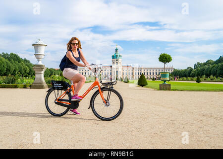 Berlin / Germany - 29 June 2018: Happy girl on rental bicycle, posing in front of Charlottenburg Palace (Schloss Charlottenburg), during a city break  Stock Photo