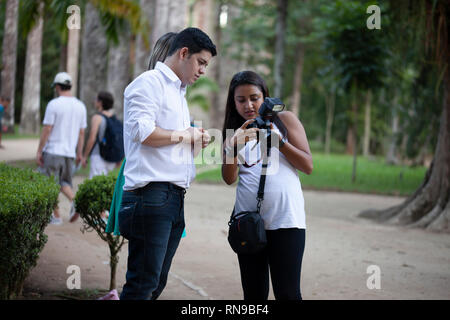 Woman photographer showing the images of a session with a couple shooting engagement images in a park with the natural surrounding in the background Stock Photo