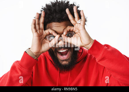 Hey smile. Portrait of friendly and optimistic playful african american adult with beard, rings and afro hairstyle wearing glasses showing okay Stock Photo