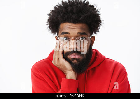 Close-up shot of lonely and gloomy upset african american man with beard and afro hairstyle in glasses leaning head on palm sighing and looking Stock Photo