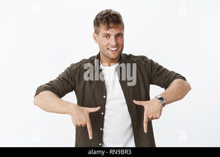 Hey check out cool place. Portrait of charismatic intriguing and handsome blond man with blue eyes and bristle smiling joyfully with hint as pointing Stock Photo