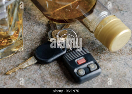 Close up  view of car keys with glass and bottle of alcohol in background.  Neutral surface. Stock Photo