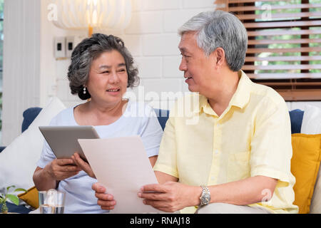 Asian senior couple use tablet searching about retirement financial document sitting on sofa at home,senior learn to use technology.aging in place con Stock Photo