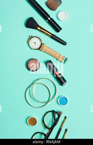 Mascara, watch, lipstick, bracelets, eyeshadow, blush, glasses and cosmetic brushes on turquoise background Stock Photo