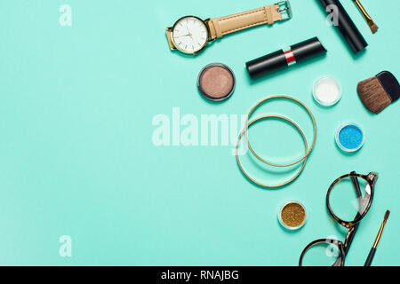Top view of mascara, watch, lipstick, bracelets, eyeshadow, blush, glasses and cosmetic brushes with copy space Stock Photo