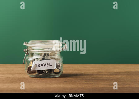glass jar with coins and lettering on wooden table and green background Stock Photo