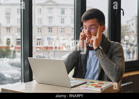 Young tired, ill, overworked man in formal wear sitting in front of computer and touching his forehead Stock Photo