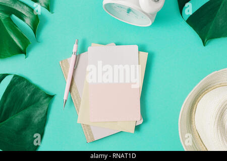 Summer background concept. Blank card with monster leaves, alarm clock and summer straw hat top view flat lay Stock Photo