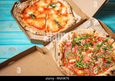 Two Carton boxes with delicious Pizza on blue wood background. Stock Photo