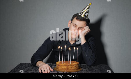 alone man celebrates a holiday, he sits alone at a table with a cake and a candles Stock Photo