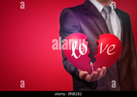 Crop image of a man in suit holding a big red broken heart with the word 'love' on red background. Stock Photo