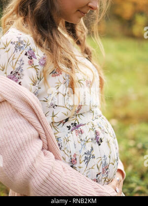 Woman holding hands with maple leaf on her pregnant belly, focus on hand Stock Photo