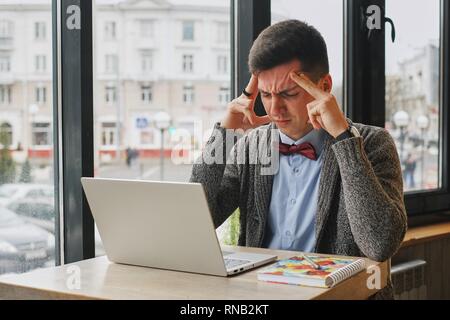 Young tired, ill, overworked man in formal wear sitting in front of computer and touching his forehead Stock Photo