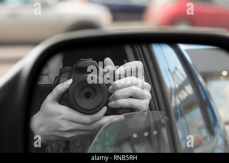 Reflection in side view mirror of someone with DSLR camera. Hidden photographing, paparazzi concept Stock Photo