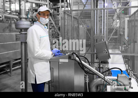 concentrated technologist taking necessary notes with help of digital tablet while standing at production department of dairy factory. The inspector c Stock Photo