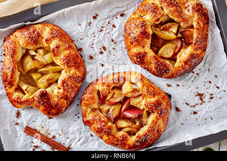 delicious open apple pies, galettes with apple slices stuffing on a baking tray,  view from above, flat lay, close-up Stock Photo