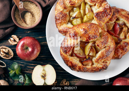 delicious open apple pies, galettes with apple slices sprinkled with sugar on a white platter. apple, cinnamon sticks, brown sugar and kitchen cloth o Stock Photo