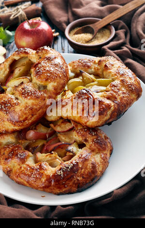 delicious open apple pies, galettes with apple slices sprinkled with sugar on a white platter. apple, cinnamon sticks, brown sugar and kitchen cloth o Stock Photo
