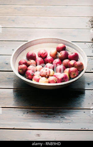 Closeup of big bowl of fresh red apples sprinkled raindrops on wooden table Stock Photo