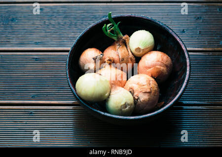 Closeup of bowl of onions sprinkled raindrops on wooden table Stock Photo