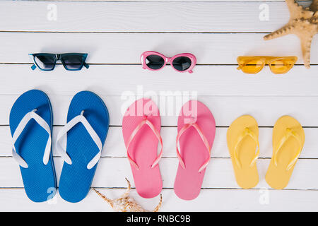 set of yellow, blue and pink sunglasses and flip flops on white wooden background Stock Photo
