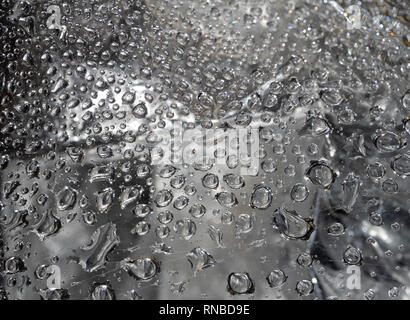 Water droplets caught on a spider web against a gray or silver background in a abstract pattern. Image has selective focus. Stock Photo