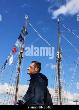 young man stands in the port on the background of the masts of ships Stock Photo