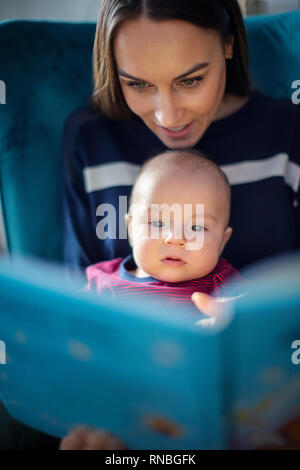 Baby Son Sitting On Mothers Lap Reading Story Book Together Stock Photo