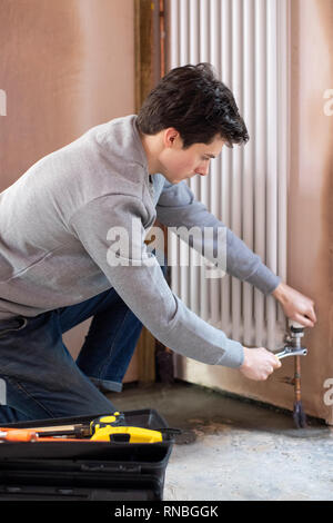 Male Plumber Fitting Vertical Radiator In Room Of House Stock Photo